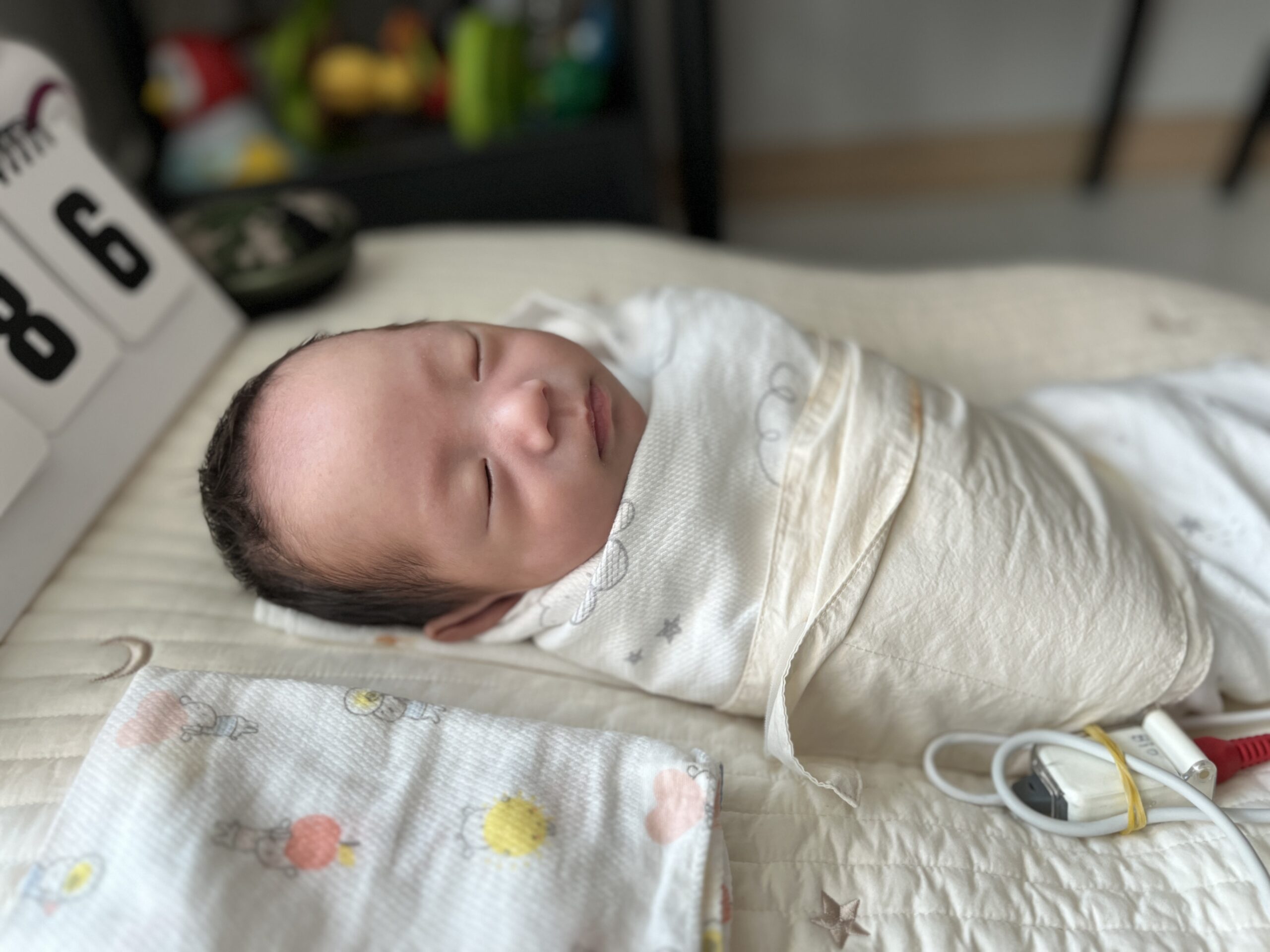 하얀색 속싸개에 단단히 싸여 등을 대고 잠든 아기 지호. 옆에는 D-DAY 달력과 아기 용품들이 놓여있다.