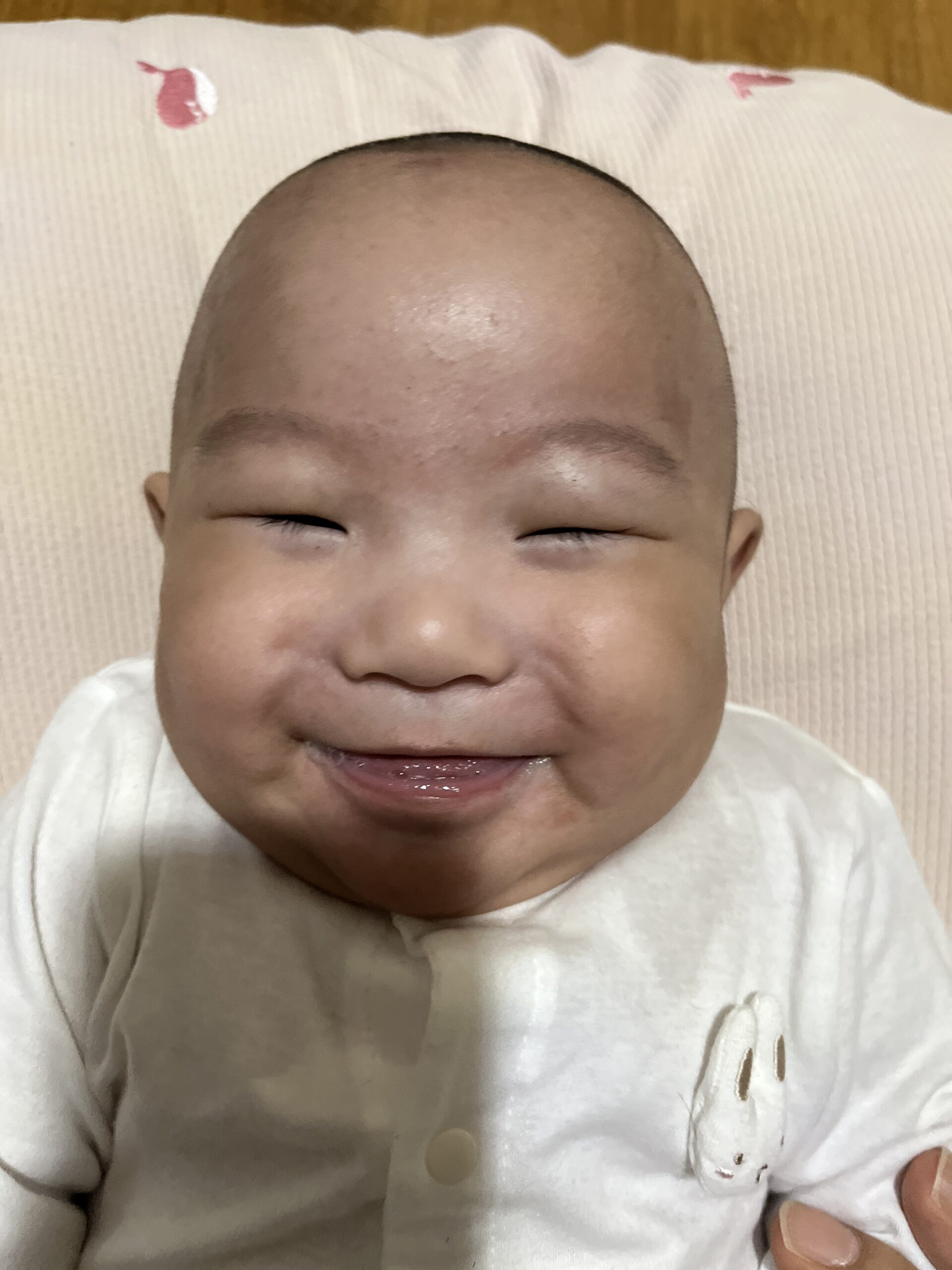 눈을 감고 활짝 웃고 있는 아기 지호의 얼굴 클로즈업 사진. 입가에 침이 살짝 묻어 있고, 흰색 긴팔 상의를 입고 있다.
