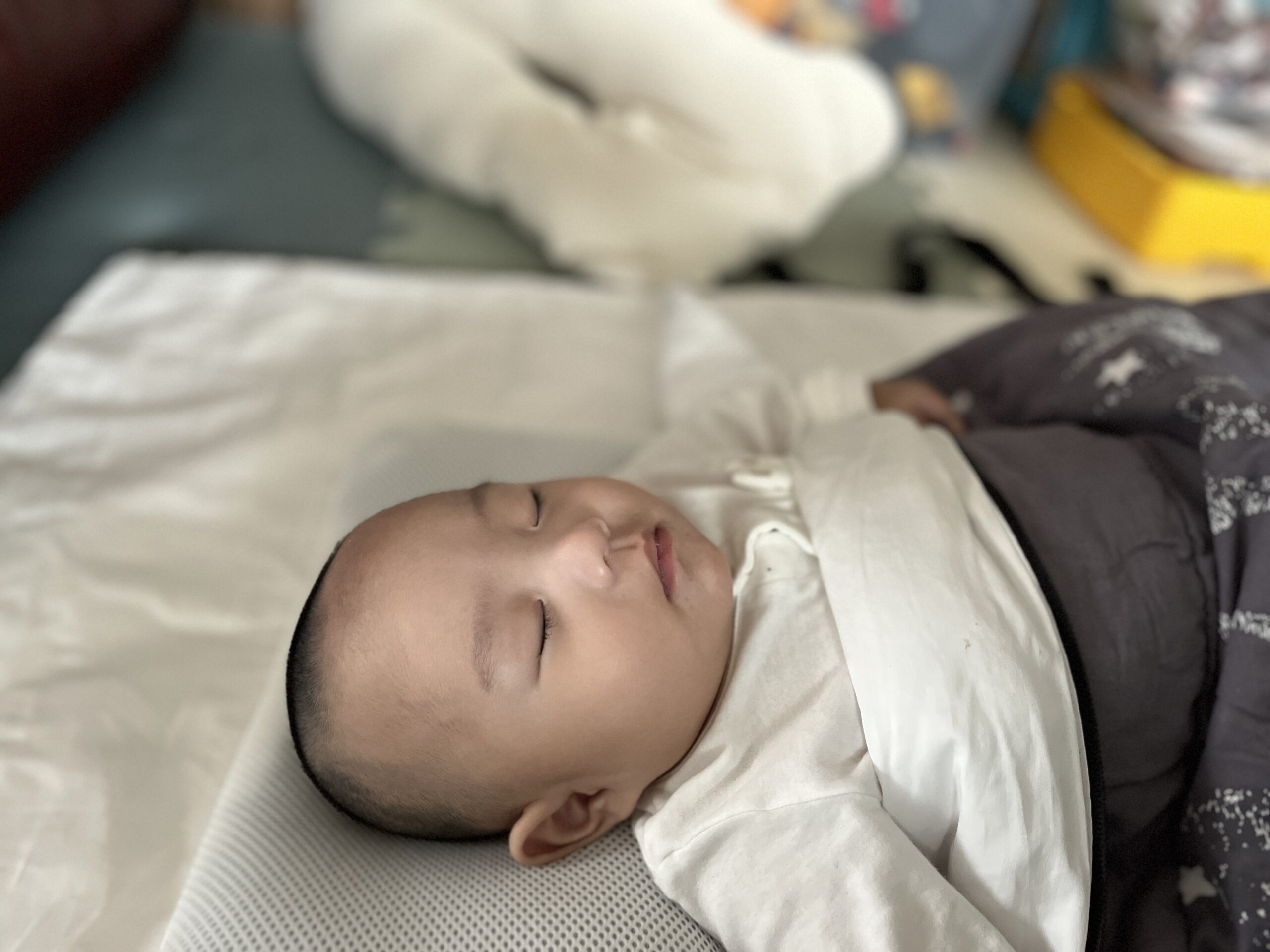 흰색 베개와 이불 위에 옆으로 누워 곤히 잠든 아기 지호의 모습. 흰색 긴팔 상의를 입고 회색 이불을 살짝 덮고 있다.
