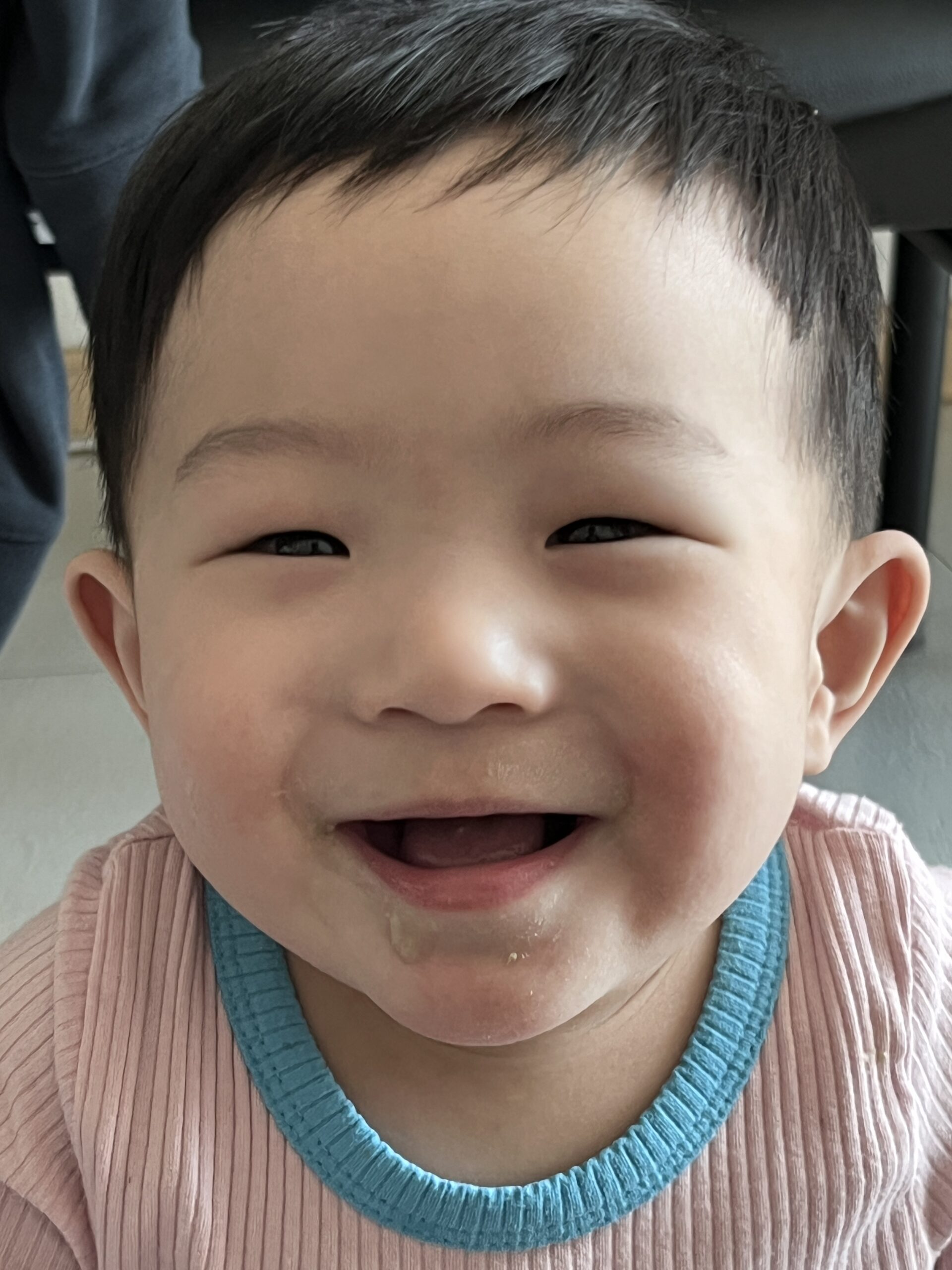 핑크색 상의를 입은 지호가 입을 크게 벌리고 눈웃음을 지으며 해맑게 웃고 있는 얼굴 클로즈업 사진. 입가에 침자국이 살짝 보인다.