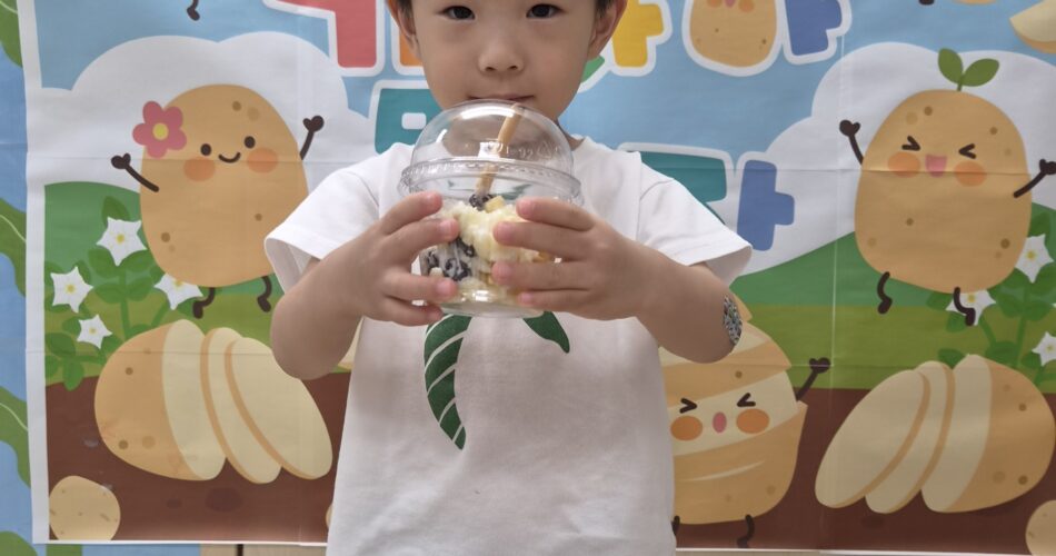 흰색 티셔츠를 입은 지호가 감자 캐릭터 배경 앞에서 투명한 컵에 담긴 샐러드를 두 손으로 들고 카메라를 응시하고 있다. 컵 안에는 과일과 감자가 섞인 듯한 내용물이 보인다.