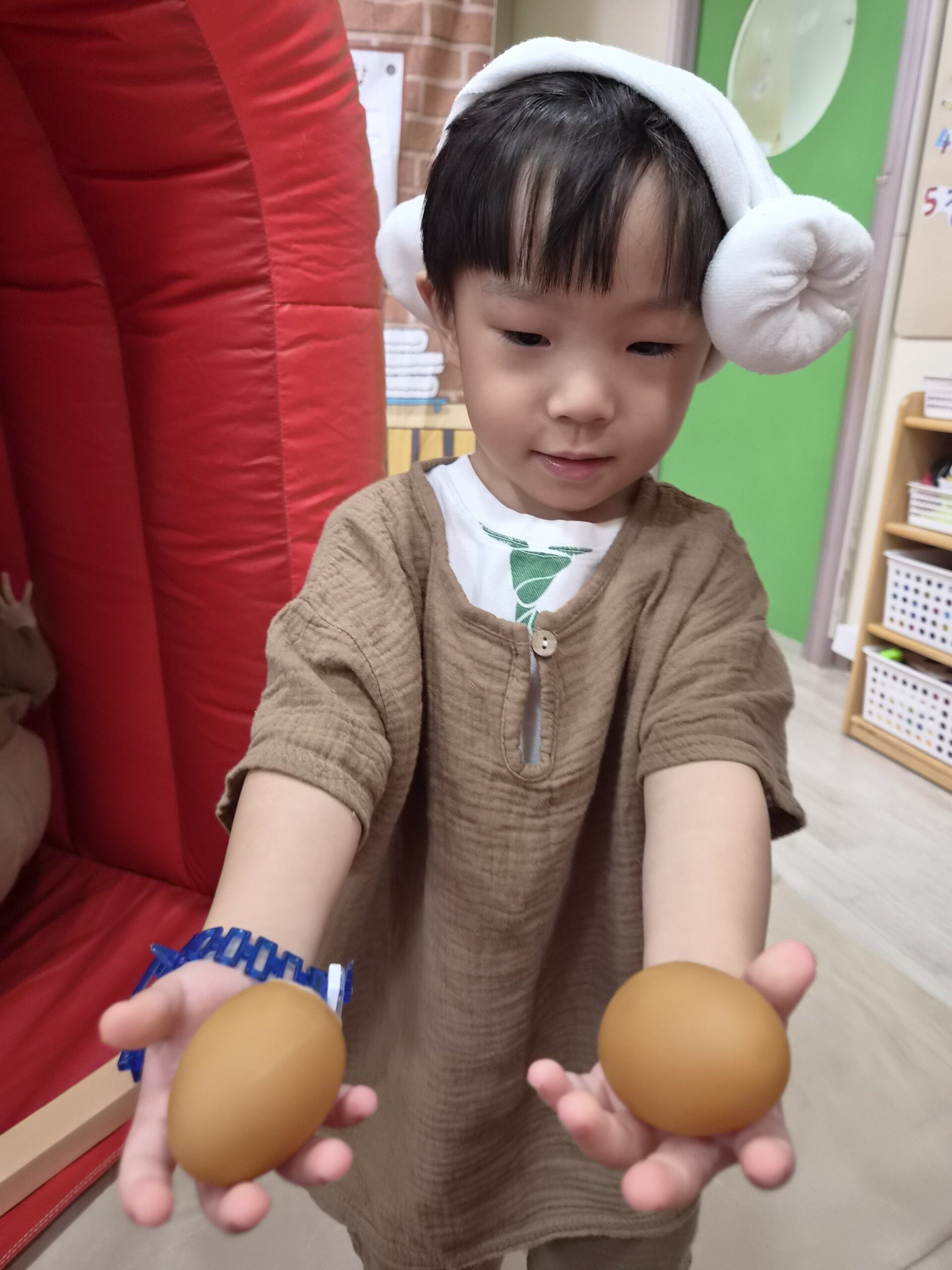 베이지색 옷과 하얀 털모자를 쓴 지호가 두 손으로 갈색 달걀 모형 두 개를 조심스럽게 들고 아래를 내려다보고 있다.